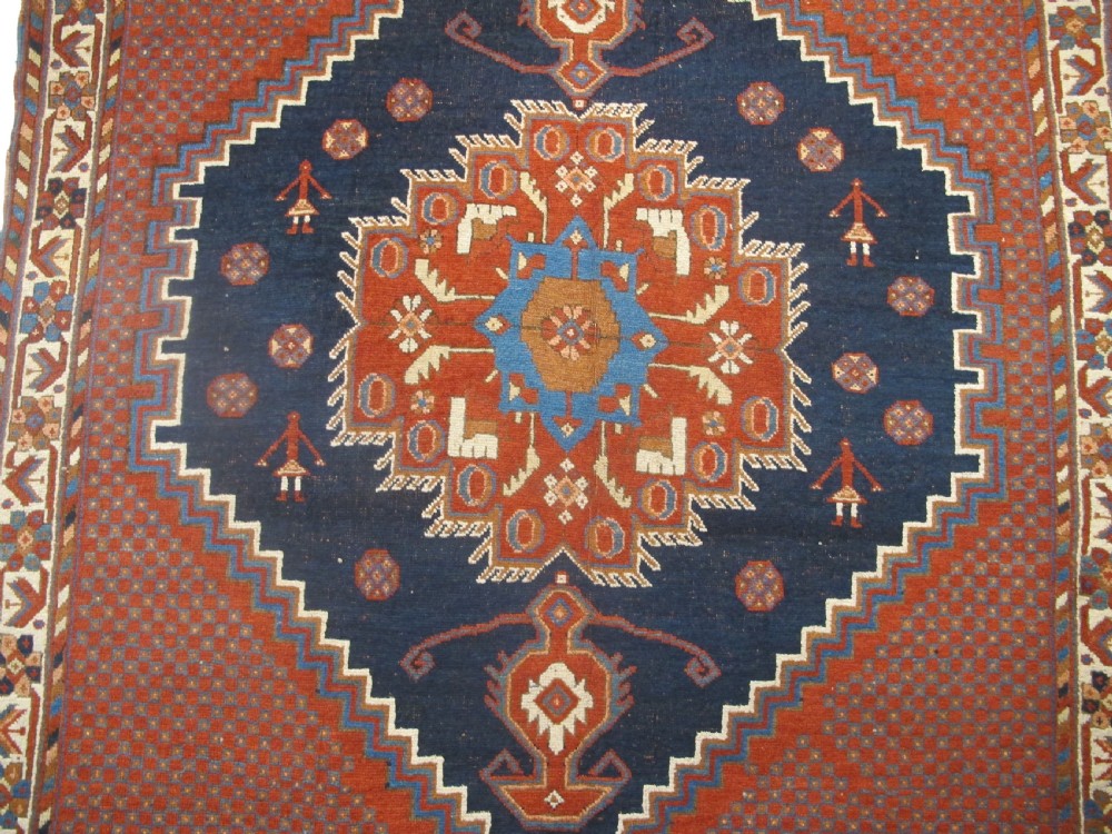 An antique Persian tribal rug featuring a central navy blue stepped medallion on a dark red geometric field, framed by stylized decorative borders. View II