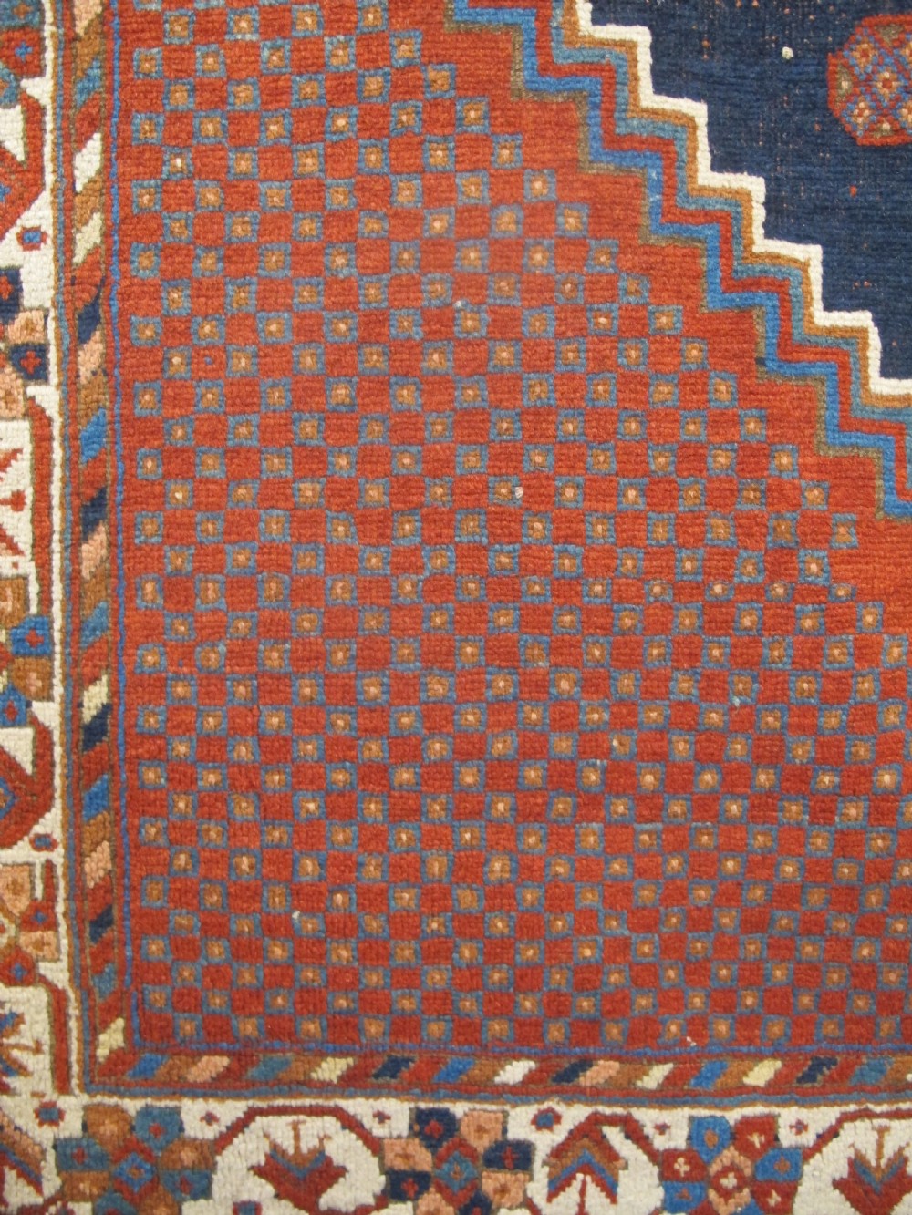 An antique Persian tribal rug featuring a central navy blue stepped medallion on a dark red geometric field, framed by stylized decorative borders. View IV