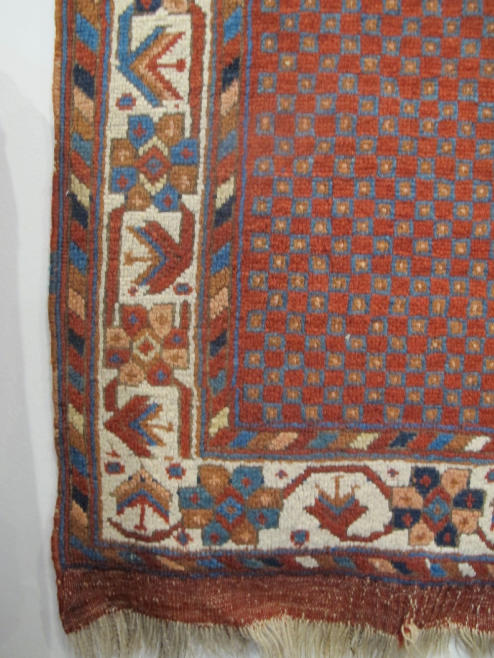An antique Persian tribal rug featuring a central navy blue stepped medallion on a dark red geometric field, framed by stylized decorative borders. View V