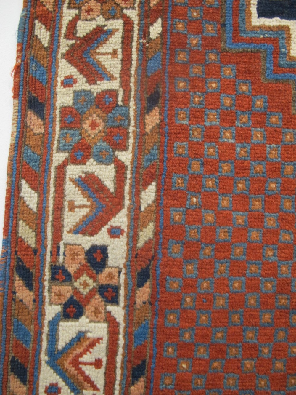 An antique Persian tribal rug featuring a central navy blue stepped medallion on a dark red geometric field, framed by stylized decorative borders. View VI