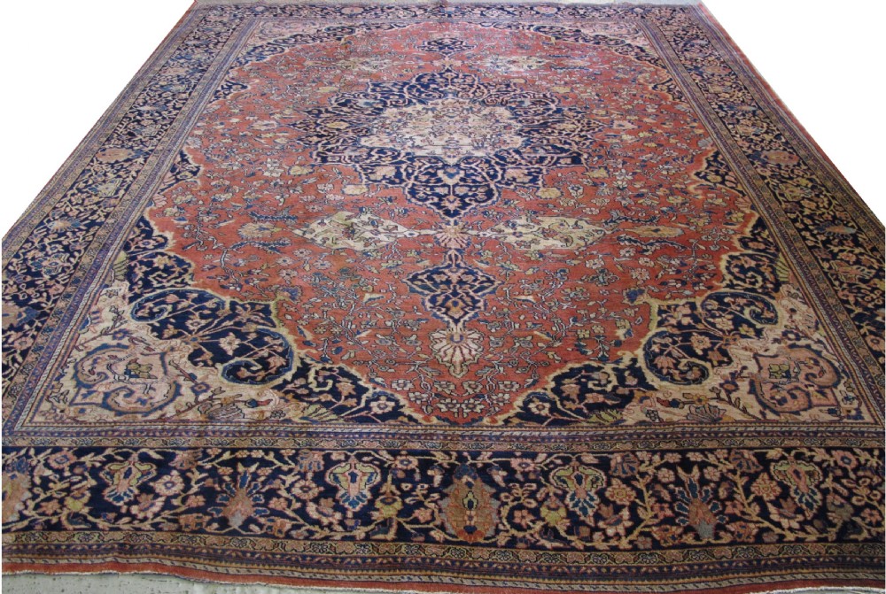 A large hand-knotted antique Persian Fereghan carpet featuring a central navy blue and ivory medallion framed by intricate floral patterns on a terracotta red field with decorative navy borders.