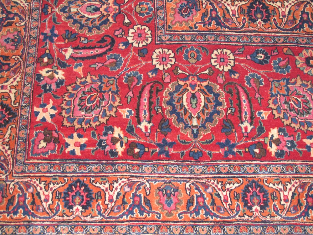 A large antique Persian wool carpet featuring a dense all-over floral pattern on a cream field framed by a wide red decorative border. View II