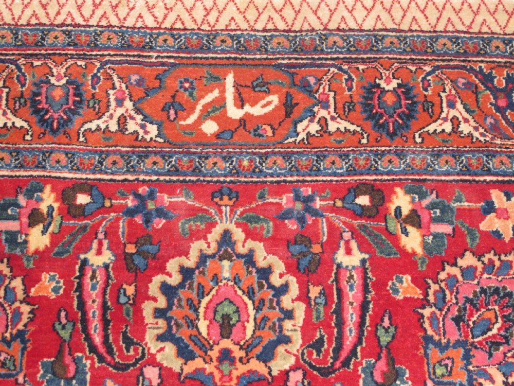 A large antique Persian wool carpet featuring a dense all-over floral pattern on a cream field framed by a wide red decorative border. View IV