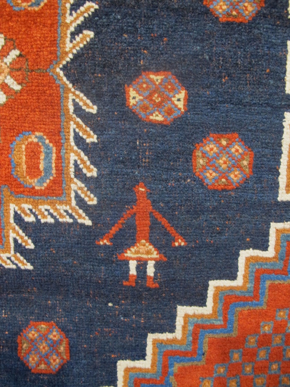 An antique Persian tribal rug featuring a central navy blue stepped medallion on a dark red geometric field, framed by stylized decorative borders. View VII
