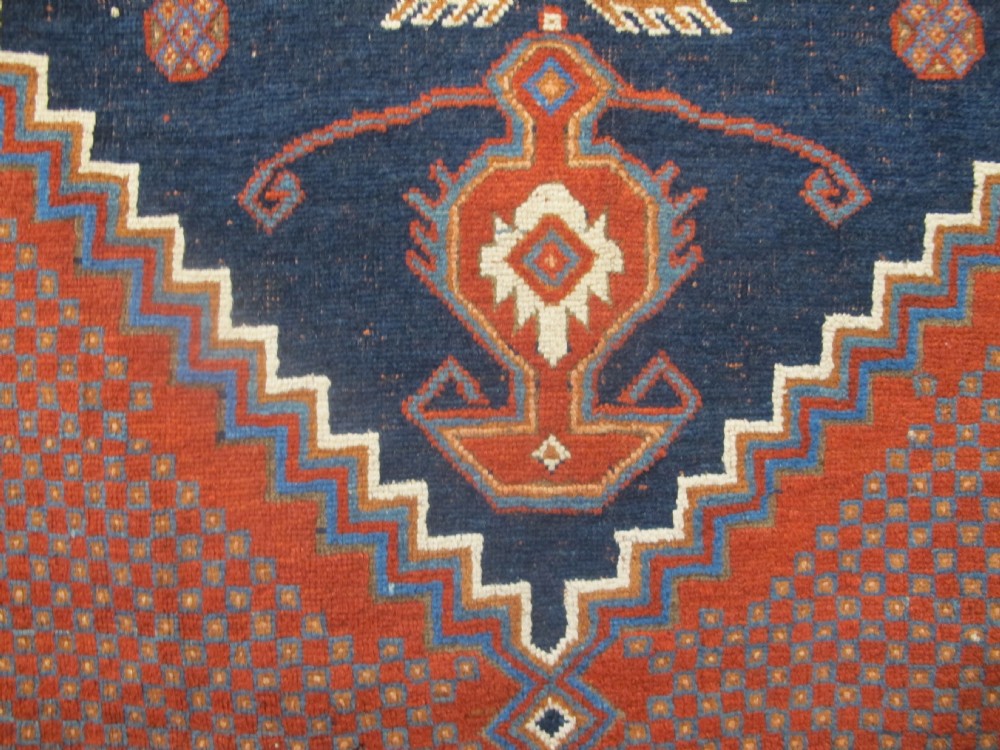 An antique Persian tribal rug featuring a central navy blue stepped medallion on a dark red geometric field, framed by stylized decorative borders. View VIII