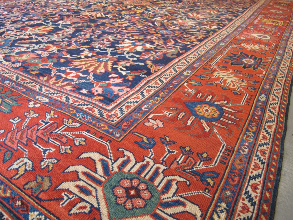 Large rectangular hand-knotted Persian Sultanabad carpet featuring a dark navy floral central field surrounded by a wide terracotta red palmette border. View VII