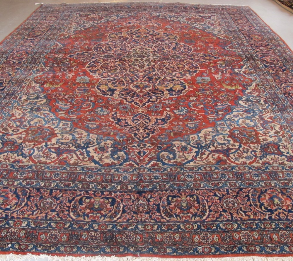 A large hand-knotted Persian Isfahan wool rug featuring a elaborate central medallion with indigo and cream arabesque floral patterns on a deep red field.