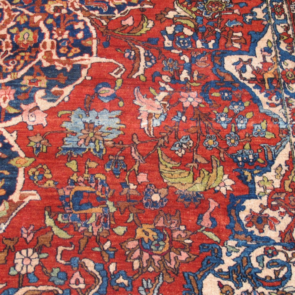 A large hand-knotted Persian Isfahan wool rug featuring a elaborate central medallion with indigo and cream arabesque floral patterns on a deep red field. View III