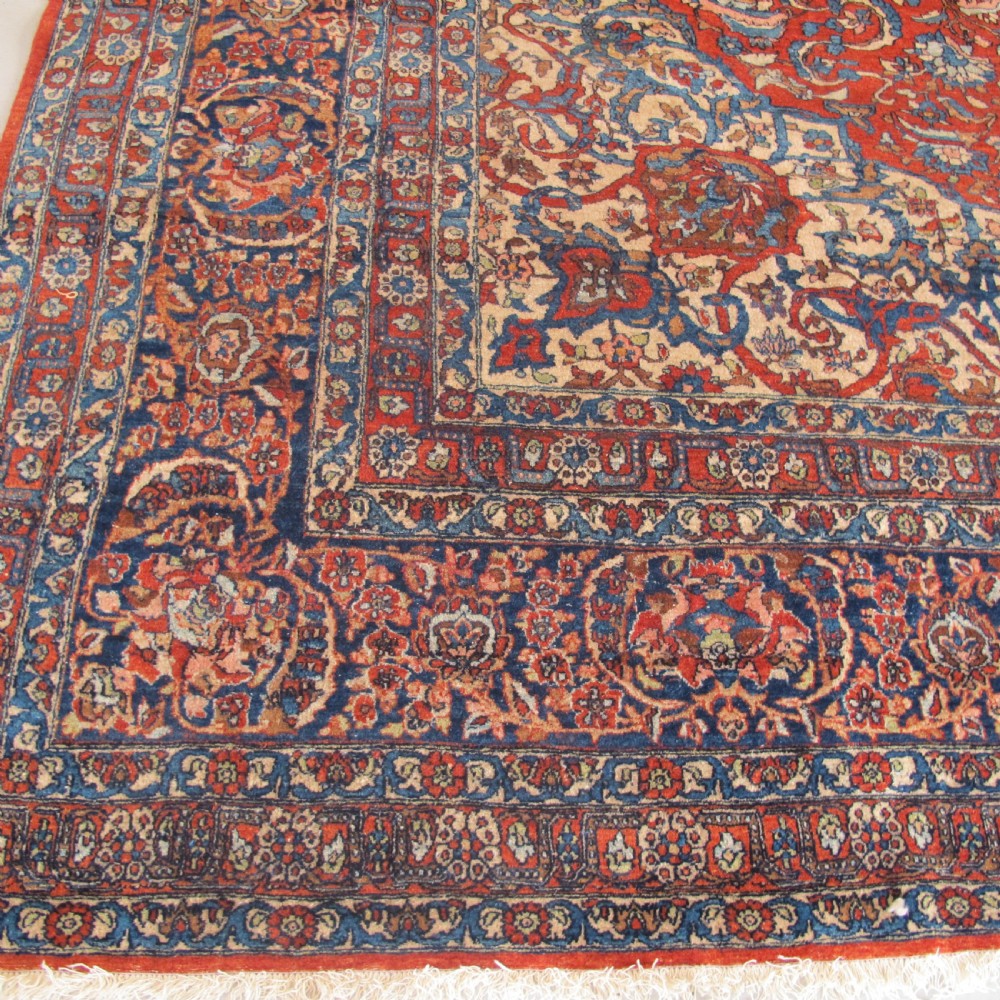 A large hand-knotted Persian Isfahan wool rug featuring a elaborate central medallion with indigo and cream arabesque floral patterns on a deep red field. View IV