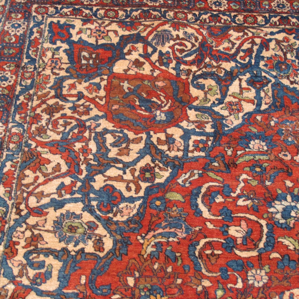 A large hand-knotted Persian Isfahan wool rug featuring a elaborate central medallion with indigo and cream arabesque floral patterns on a deep red field. View VI