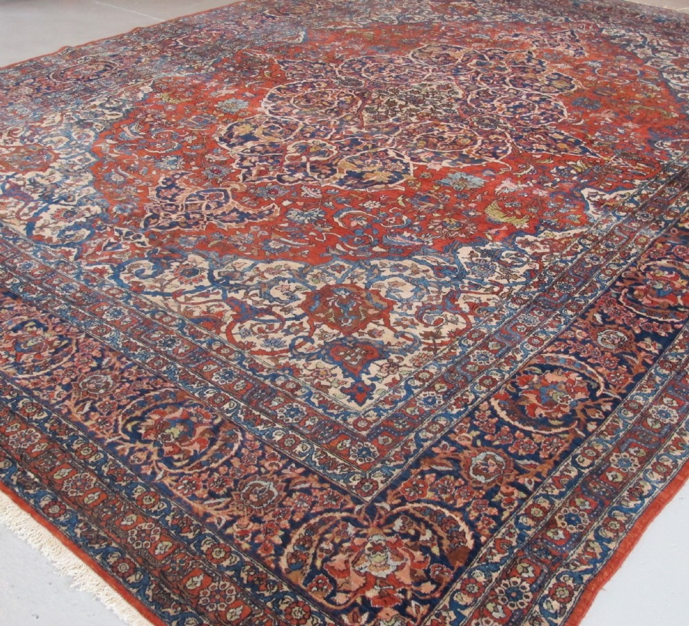 A large hand-knotted Persian Isfahan wool rug featuring a elaborate central medallion with indigo and cream arabesque floral patterns on a deep red field. View VII
