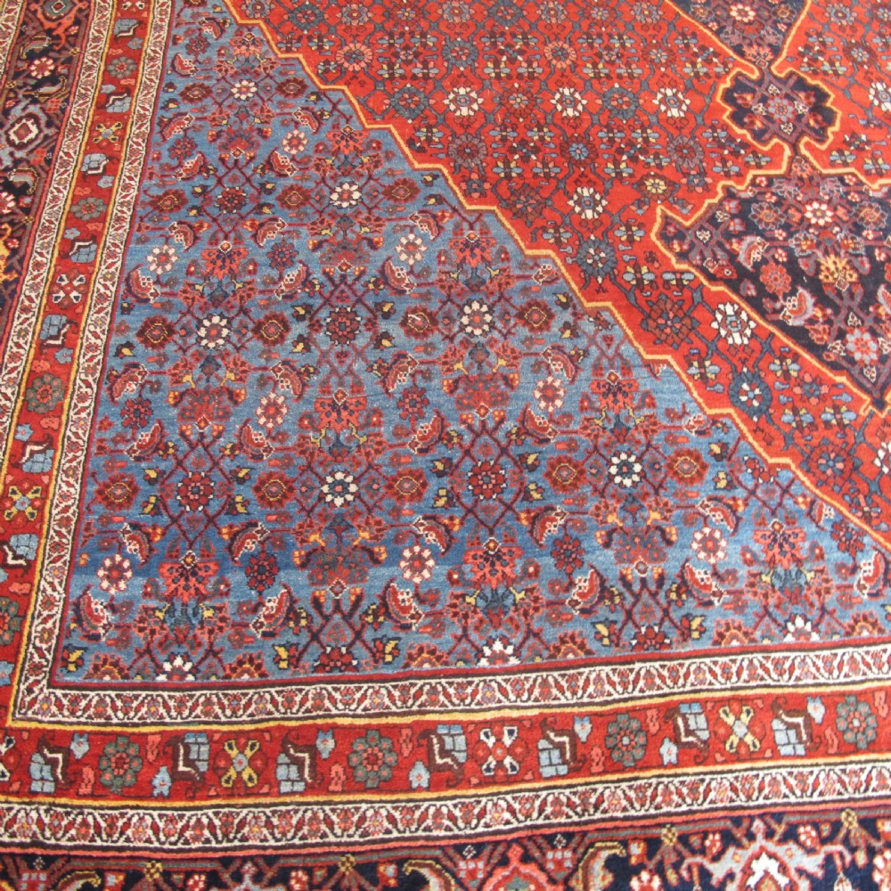 A large antique Persian Bidjar carpet featuring a central diamond medallion, red field, blue spandrels, and intricate floral borders. View II