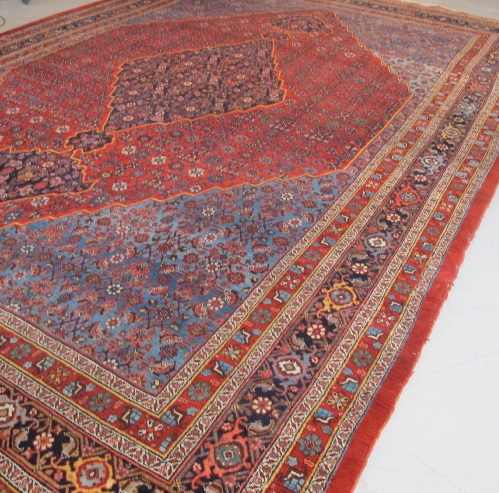 A large antique Persian Bidjar carpet featuring a central diamond medallion, red field, blue spandrels, and intricate floral borders. View III