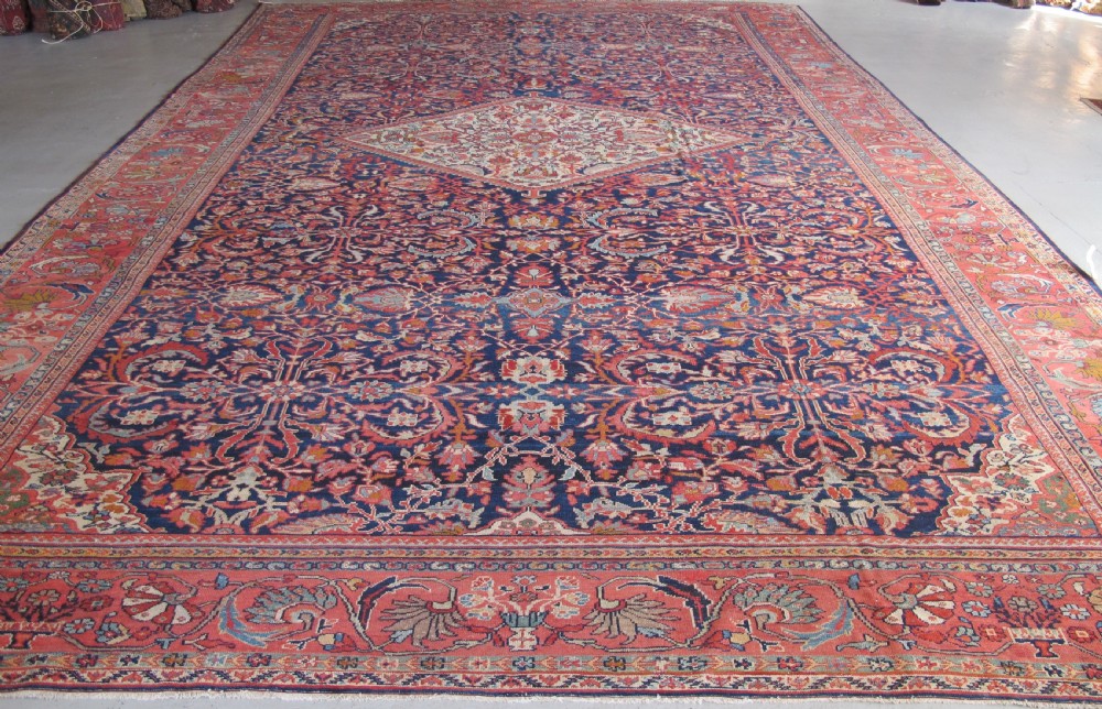 A large palace-sized antique Persian Sultanabad wool carpet featuring a deep navy blue central field, an ivory diamond medallion, intricate floral arabesques, and a broad terracotta border.