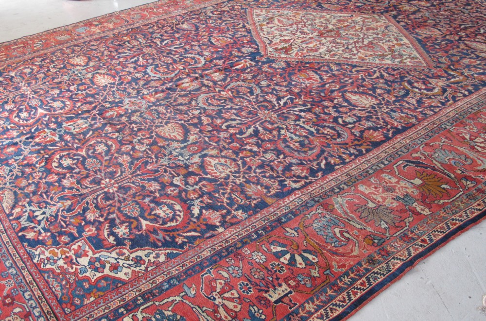 A large palace-sized antique Persian Sultanabad wool carpet featuring a deep navy blue central field, an ivory diamond medallion, intricate floral arabesques, and a broad terracotta border. View V