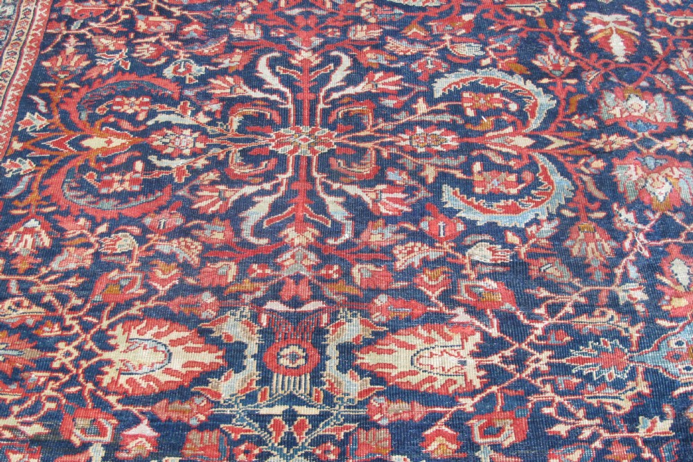 A large palace-sized antique Persian Sultanabad wool carpet featuring a deep navy blue central field, an ivory diamond medallion, intricate floral arabesques, and a broad terracotta border. View VI