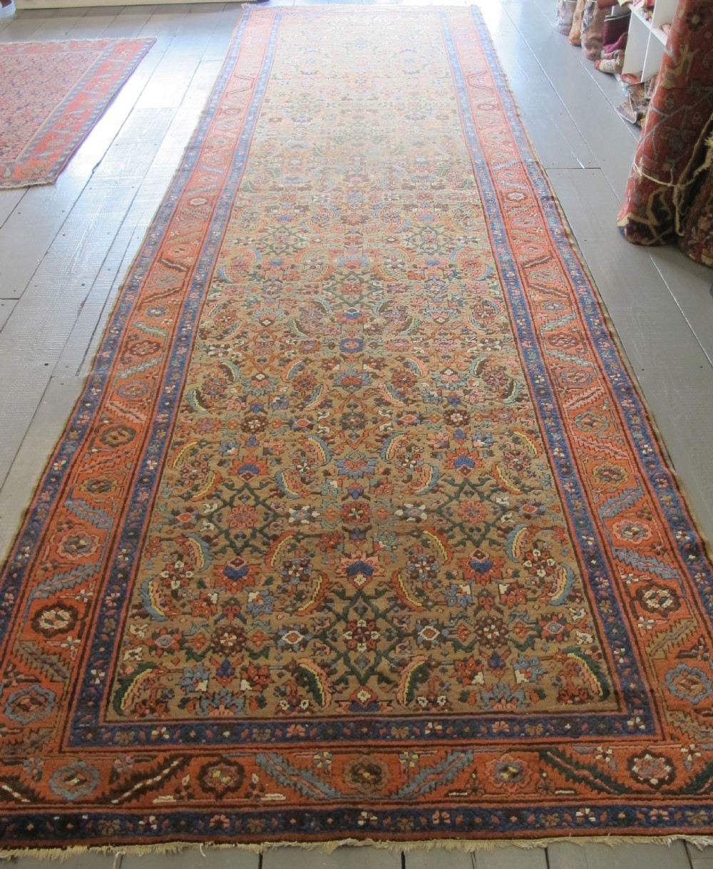 A long hand-knotted antique North-West Persian gallery carpet featuring detailed floral patterns on a camel field with terracotta borders.
