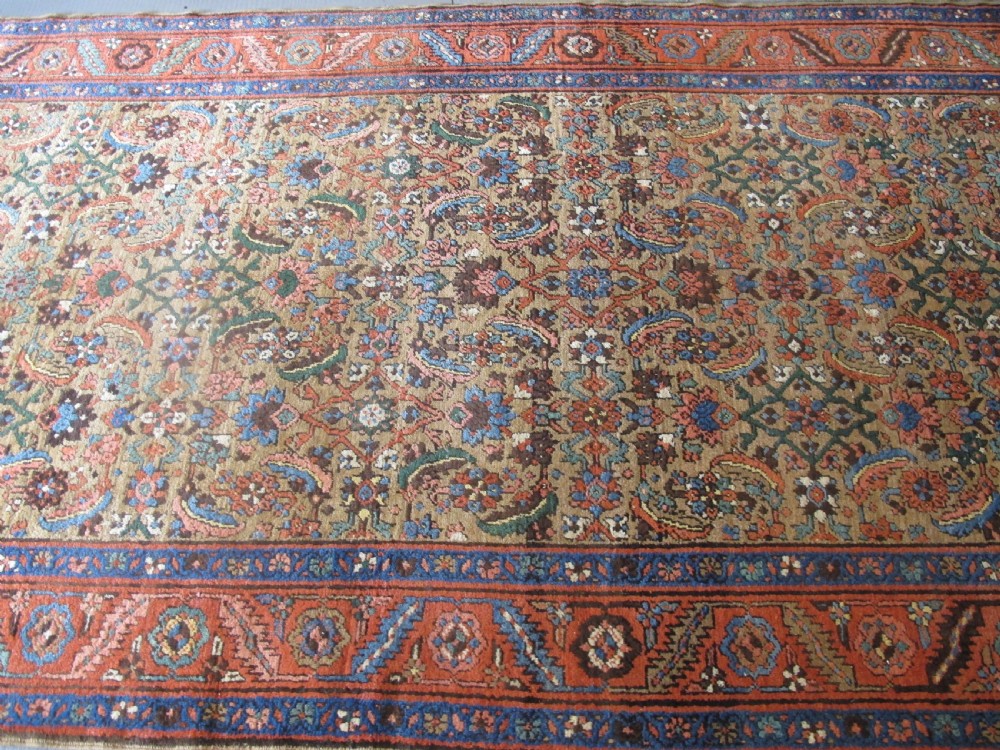 A long hand-knotted antique North-West Persian gallery carpet featuring detailed floral patterns on a camel field with terracotta borders. View X