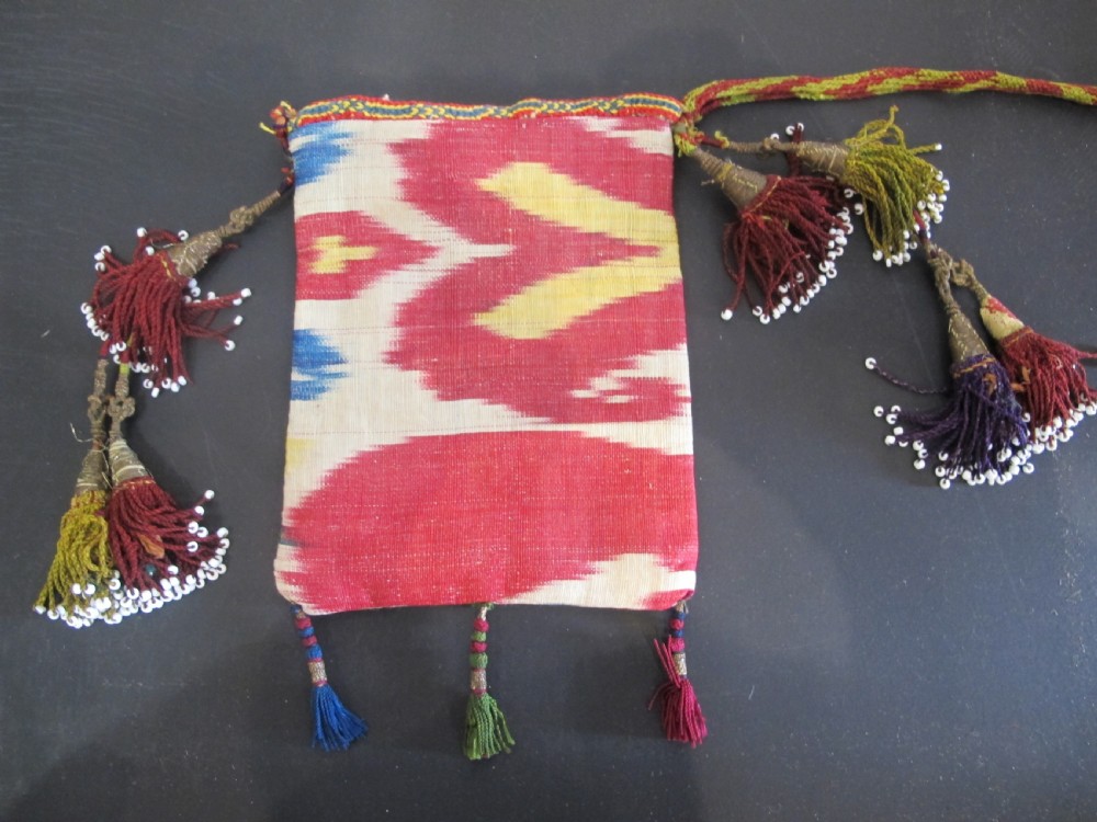 A double-sided silk ikat purse from Uzbekistan featuring red, yellow, and cream abstract patterns with braided shoulder straps and beaded tassels. View II