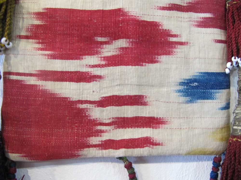 A double-sided silk ikat purse from Uzbekistan featuring red, yellow, and cream abstract patterns with braided shoulder straps and beaded tassels. View IV