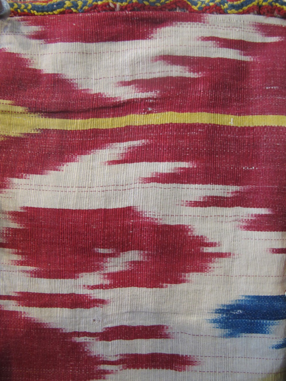 A double-sided silk ikat purse from Uzbekistan featuring red, yellow, and cream abstract patterns with braided shoulder straps and beaded tassels. View VI