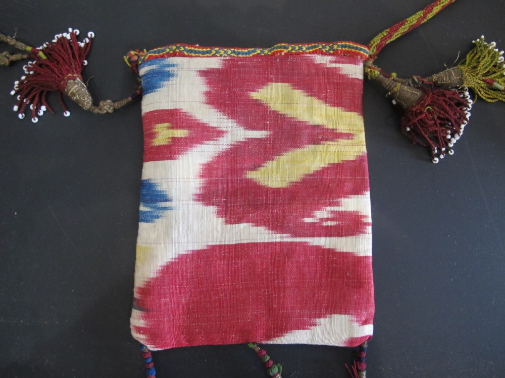 A double-sided silk ikat purse from Uzbekistan featuring red, yellow, and cream abstract patterns with braided shoulder straps and beaded tassels. View VII