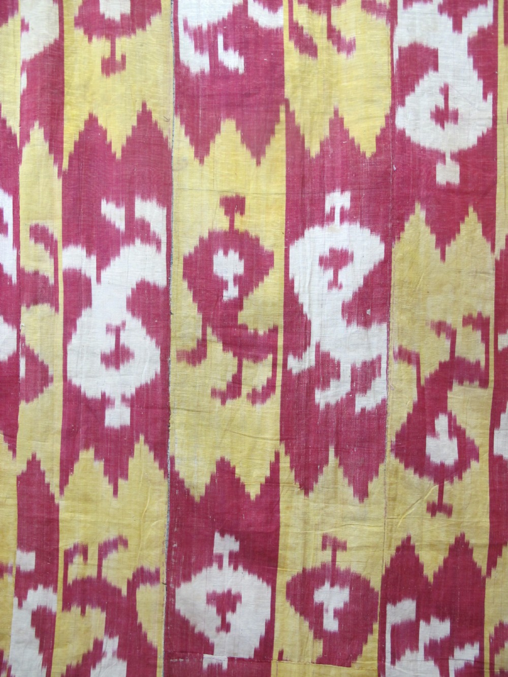 An antique Uzbek handwoven silk ikat panel with repeating vertical geometric and abstract cloud motifs in crimson, yellow, and off-white. View II