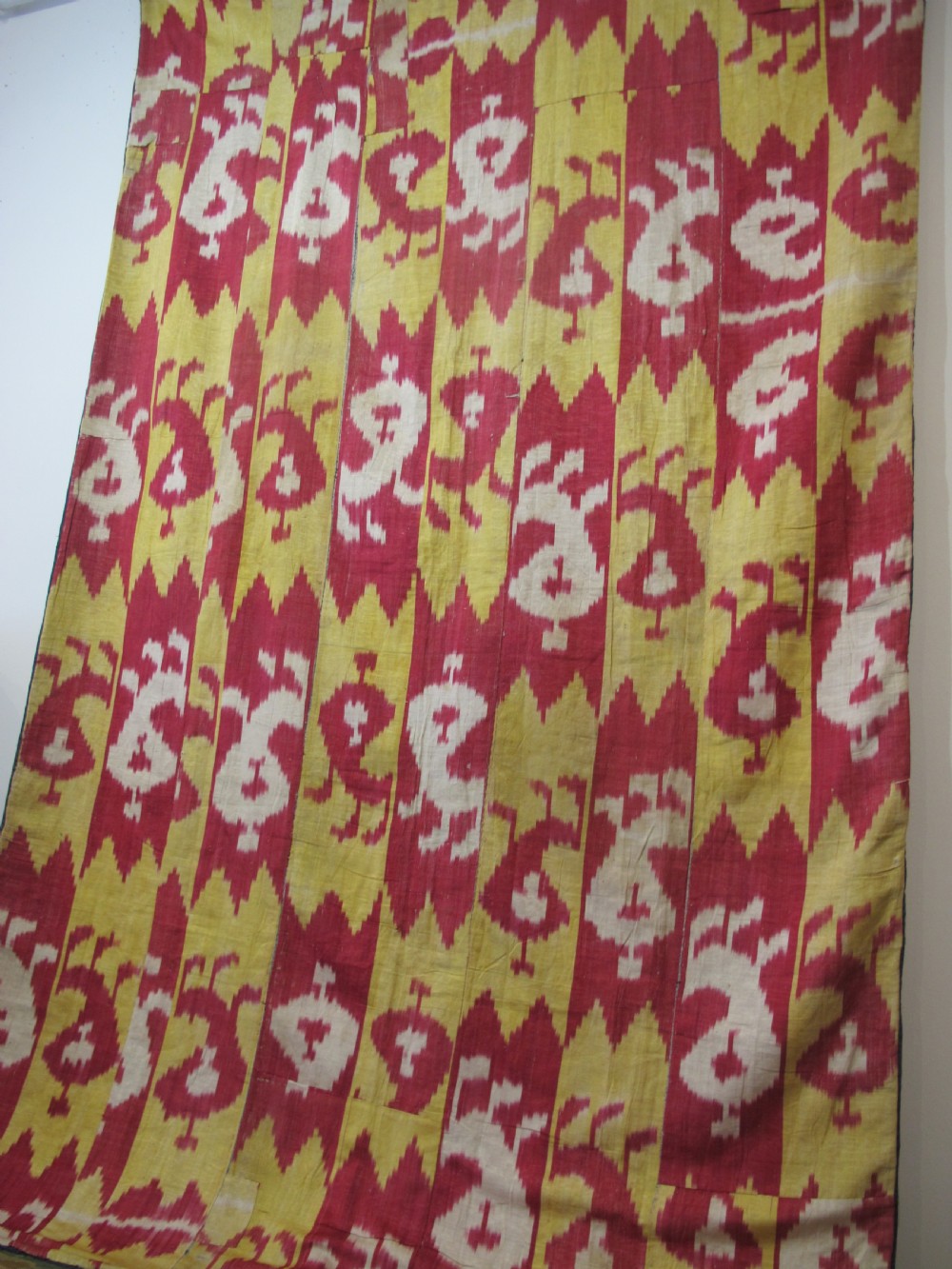 An antique Uzbek handwoven silk ikat panel with repeating vertical geometric and abstract cloud motifs in crimson, yellow, and off-white. View VII