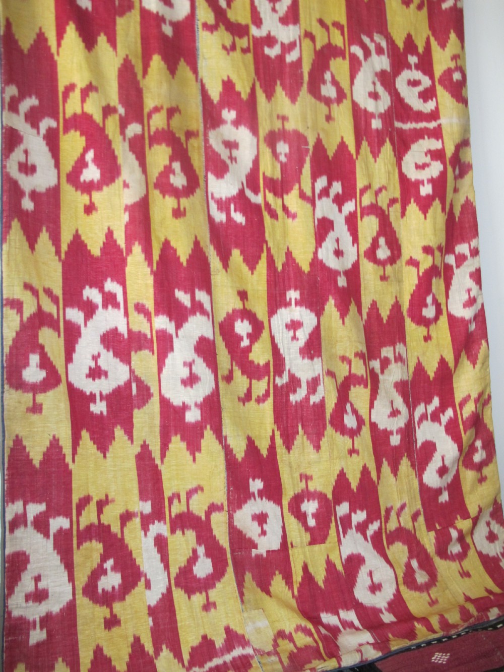 An antique Uzbek handwoven silk ikat panel with repeating vertical geometric and abstract cloud motifs in crimson, yellow, and off-white. View IX