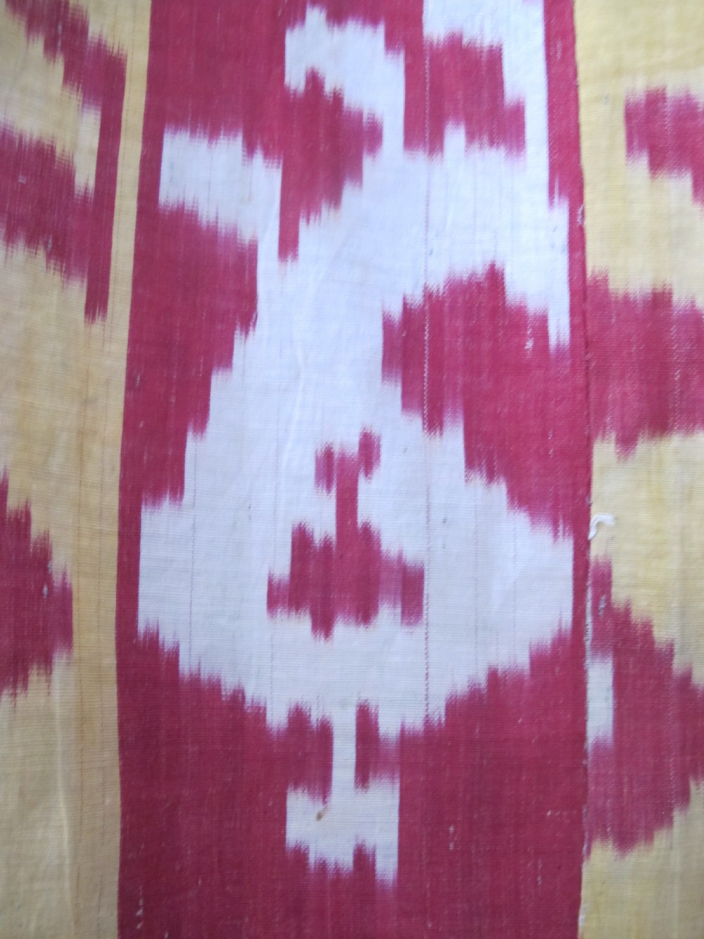 An antique Uzbek handwoven silk ikat panel with repeating vertical geometric and abstract cloud motifs in crimson, yellow, and off-white. View X