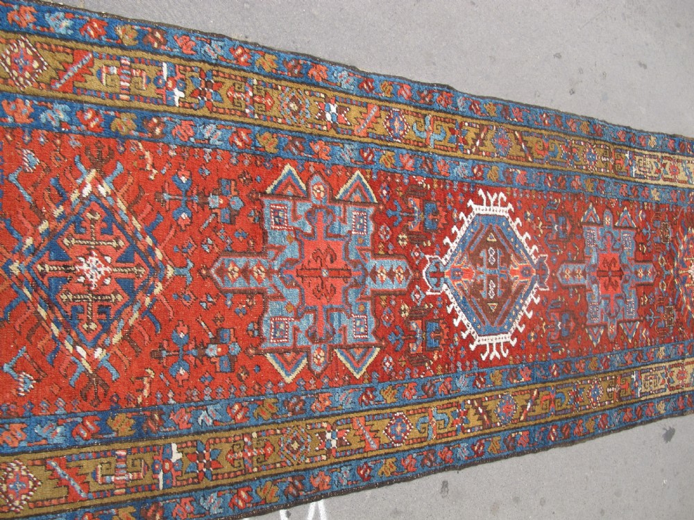 A long hand-knotted Persian Heriz wool runner rug featuring geometric medallions in shades of red, blue, and gold against a red field. View IV