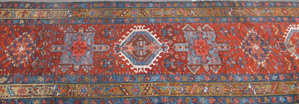 A long hand-knotted Persian Heriz wool runner rug featuring geometric medallions in shades of red, blue, and gold against a red field. View VI
