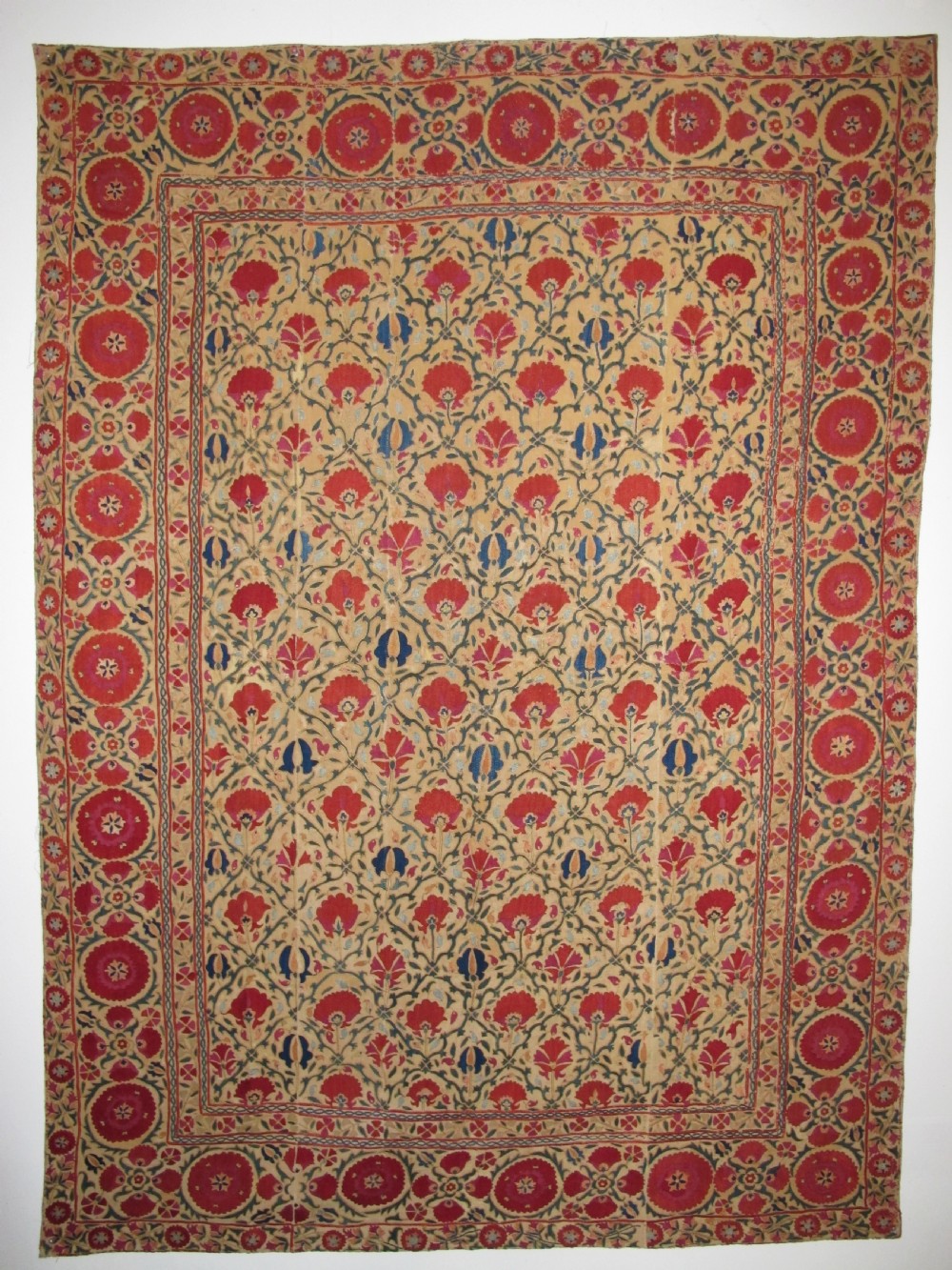 A 19th-century Bokhara suzani textile featuring red silk floral embroidery on a cream cotton ground surrounded by a wide rosette border.