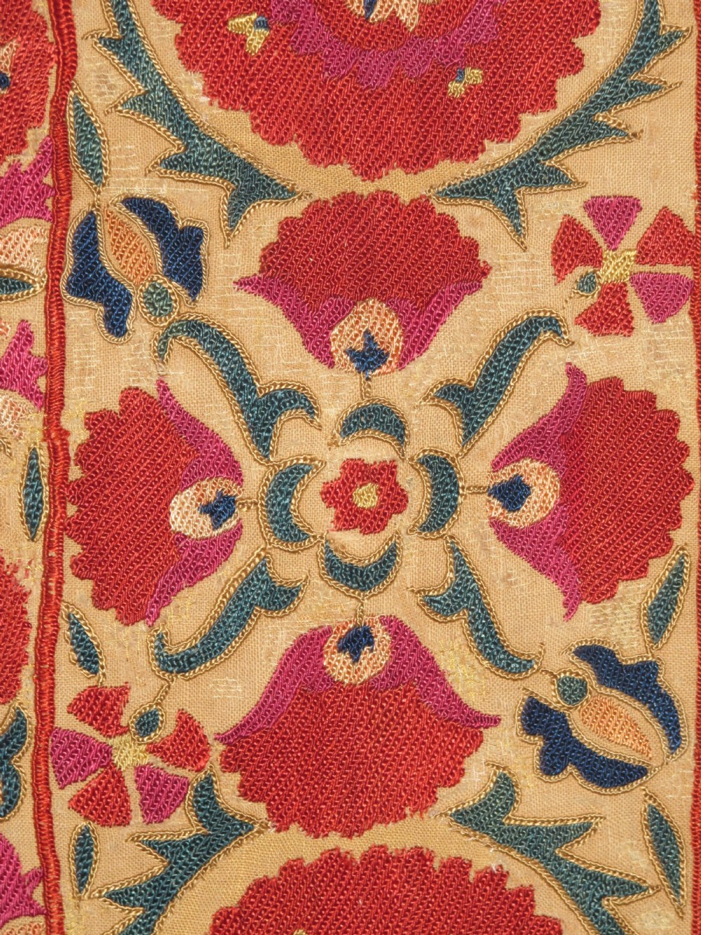 A 19th-century Bokhara suzani textile featuring red silk floral embroidery on a cream cotton ground surrounded by a wide rosette border. View III