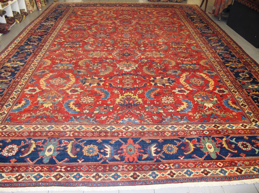 A large hand-knotted Persian Sultanabad wool carpet featuring a red central field filled with floral motifs and bordered by a wide navy band.