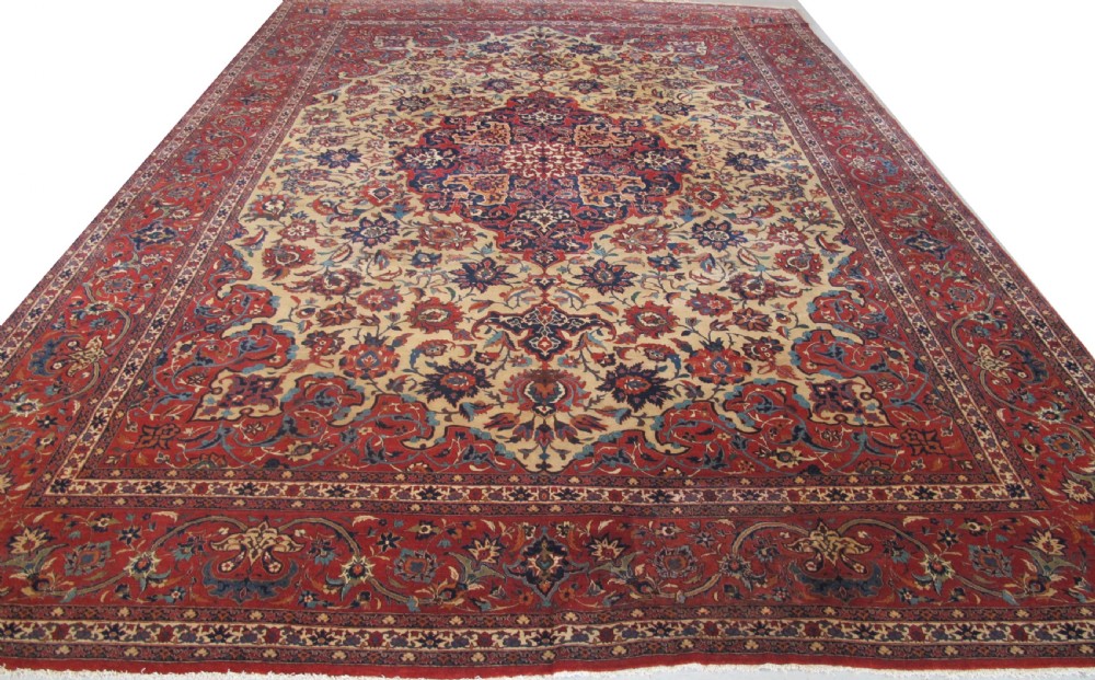 A large hand-knotted Persian Isfahan carpet featuring a central dark blue and red medallion on an ivory ground with a wide crimson floral border.