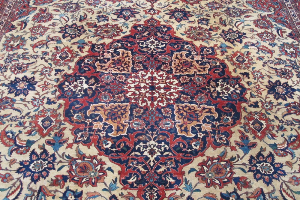 A large hand-knotted Persian Isfahan carpet featuring a central dark blue and red medallion on an ivory ground with a wide crimson floral border. View III
