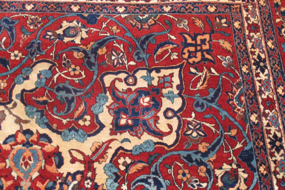 A large hand-knotted Persian Isfahan carpet featuring a central dark blue and red medallion on an ivory ground with a wide crimson floral border. View IV