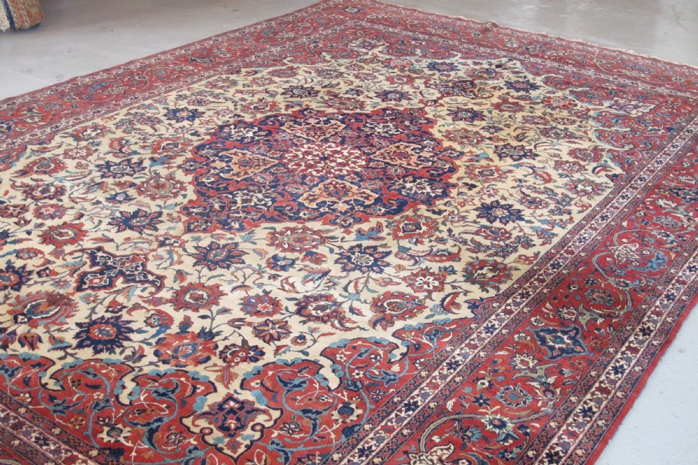 A large hand-knotted Persian Isfahan carpet featuring a central dark blue and red medallion on an ivory ground with a wide crimson floral border. View VI