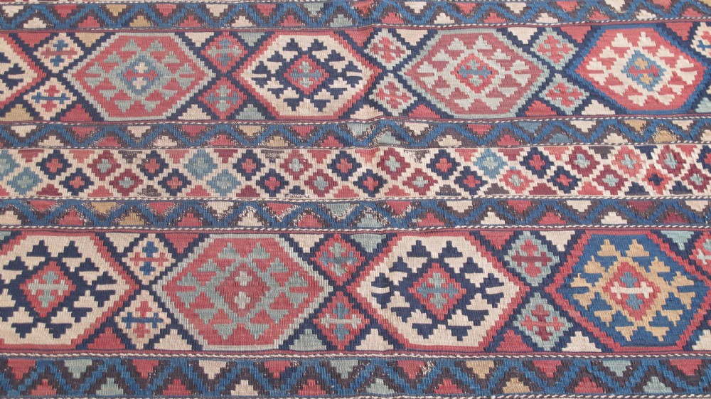 An antique 19th-century flat-woven Caucasian kilim rug featuring horizontal bands filled with geometric diamond and hexagon patterns in terracotta, indigo, ochre, and cream. View II