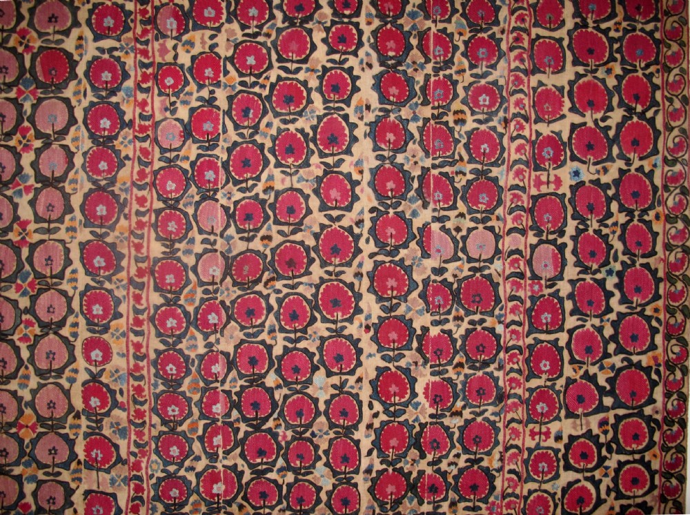A large rectangular antique suzani textile featuring repeating circular red floral motifs framed by a decorative floral border on an off-white ground. View II