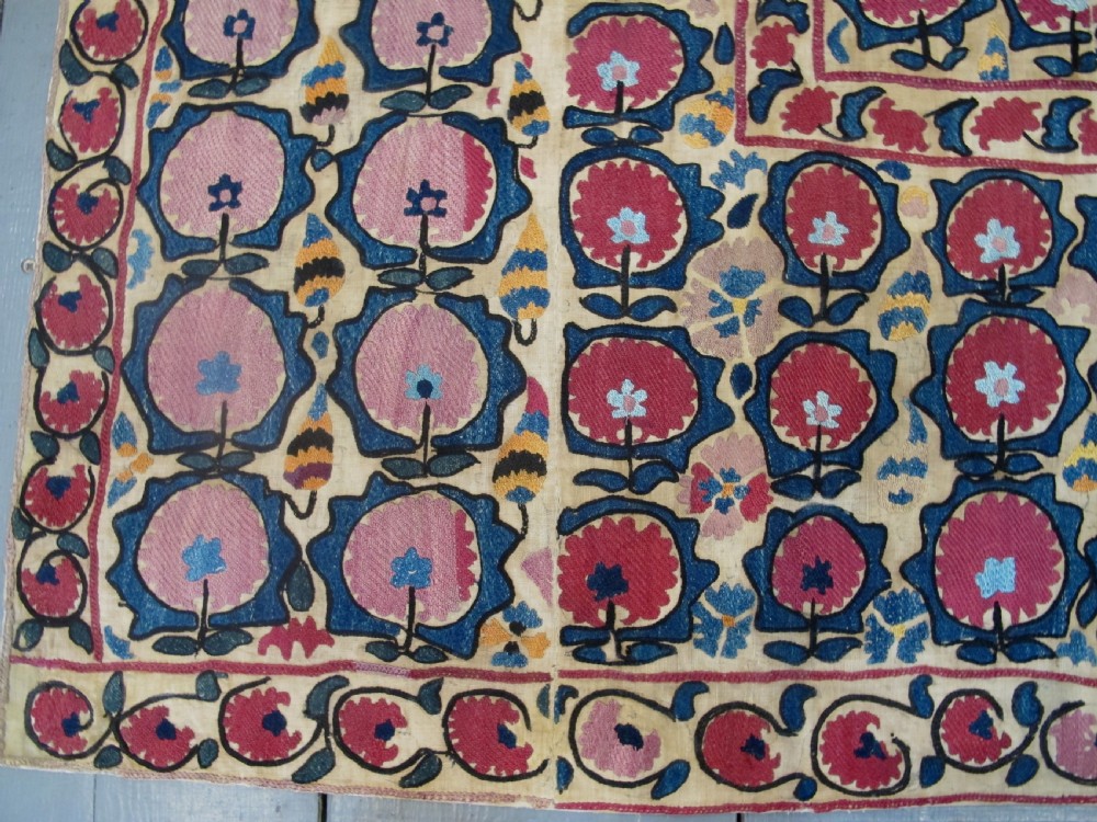 A large rectangular antique suzani textile featuring repeating circular red floral motifs framed by a decorative floral border on an off-white ground. View III