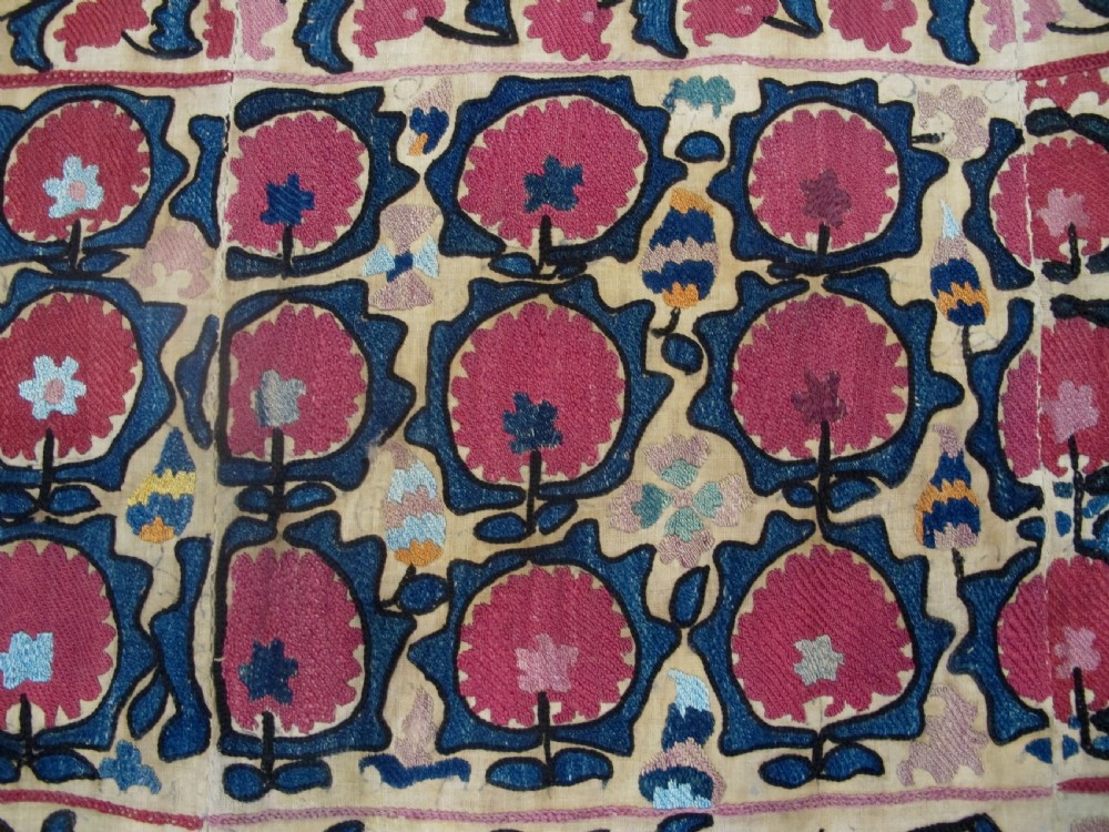 A large rectangular antique suzani textile featuring repeating circular red floral motifs framed by a decorative floral border on an off-white ground. View IV