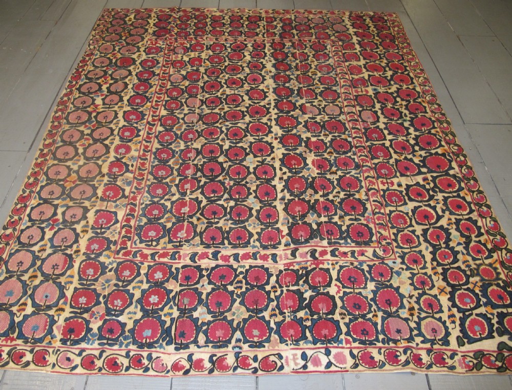 A large rectangular antique suzani textile featuring repeating circular red floral motifs framed by a decorative floral border on an off-white ground. View VI
