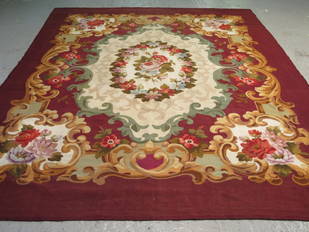 A rectangular flatweave Aubusson wool carpet featuring a central floral medallion surrounded by acanthus scrollwork cartouches on a deep red ground.