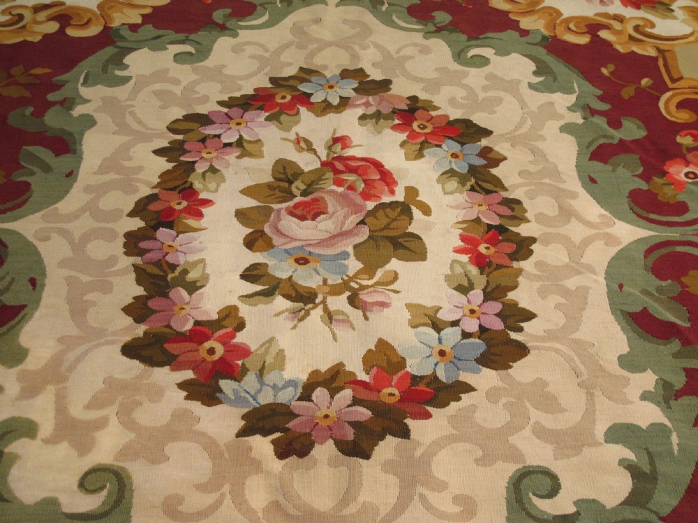 A rectangular flatweave Aubusson wool carpet featuring a central floral medallion surrounded by acanthus scrollwork cartouches on a deep red ground. View II