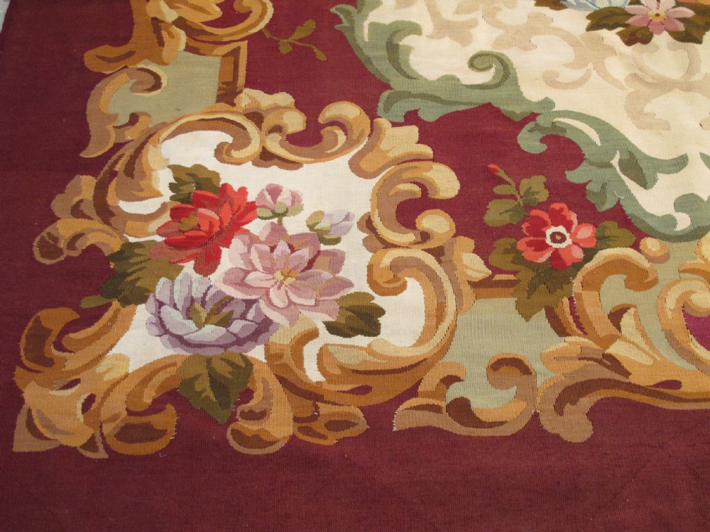 A rectangular flatweave Aubusson wool carpet featuring a central floral medallion surrounded by acanthus scrollwork cartouches on a deep red ground. View III