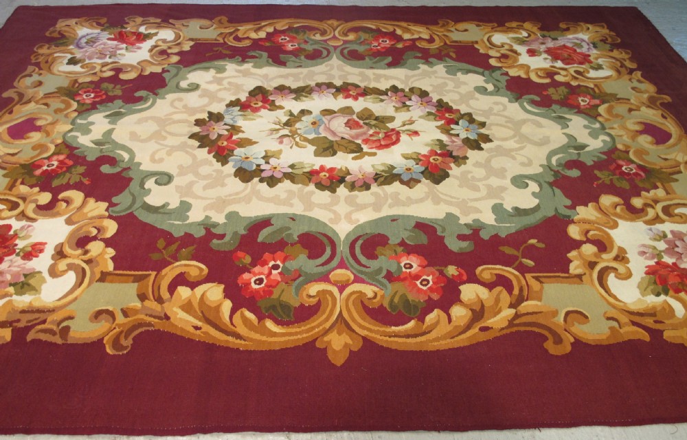 A rectangular flatweave Aubusson wool carpet featuring a central floral medallion surrounded by acanthus scrollwork cartouches on a deep red ground. View V