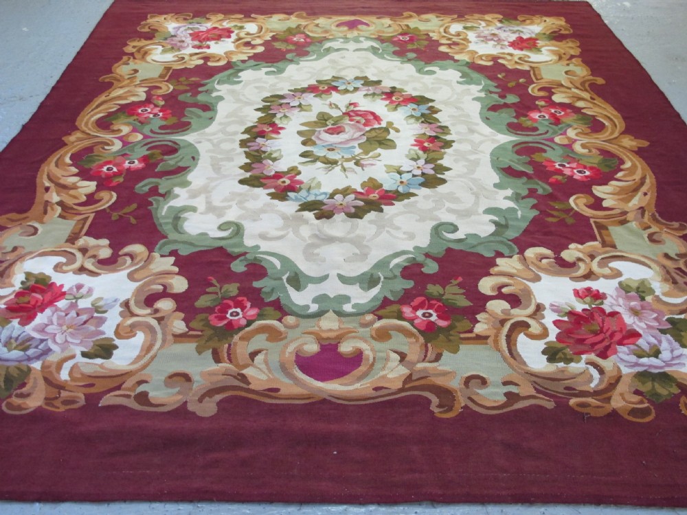 A rectangular flatweave Aubusson wool carpet featuring a central floral medallion surrounded by acanthus scrollwork cartouches on a deep red ground. View VI