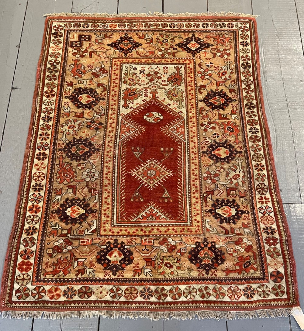 A rectangular hand-knotted Anatolian Melas wool rug featuring a red central pointed mihrab field framed by broad geometric patterned borders in cream, ochre, and dark brown.